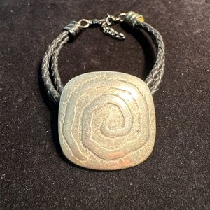 A leather braided bracelet featuring a silver-toned spiral medallion.